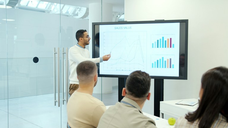 Man presenting charts on a large screen to audience